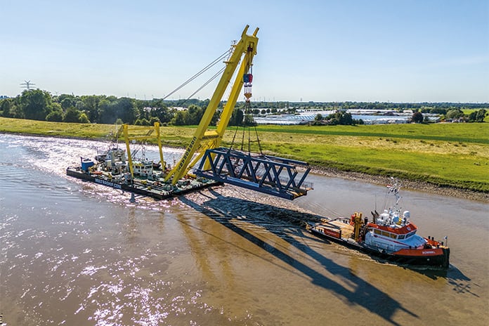 schwimmender Kran wird von einem Boot gezogen und transportiert einen Teil einer Brücke über den Fluss