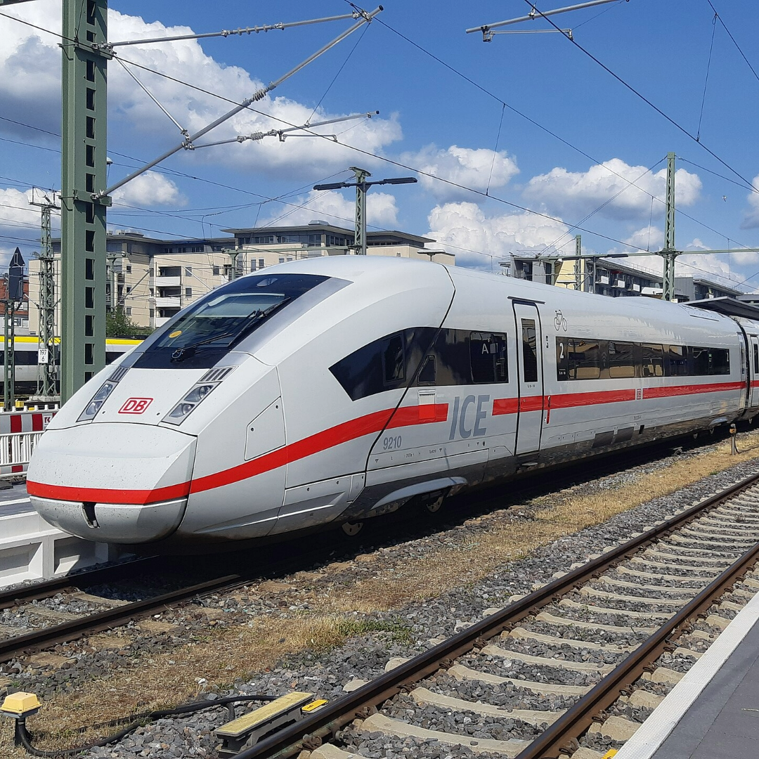 Ein moderner ICE-Zug der Deutschen Bahn steht an einem Gleis im Bahnhof Friedrichshafen Stadt. Der Zug ist weiß mit einem markanten roten Streifen und trägt das DB-Logo sowie die Aufschrift 