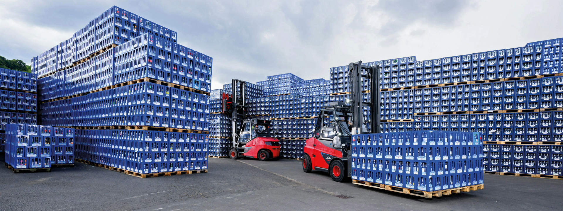 Zwei rote Gabelstapler transportieren Paletten mit blauen Gerolsteiner Wasserkästen in einem großen Außenlager.