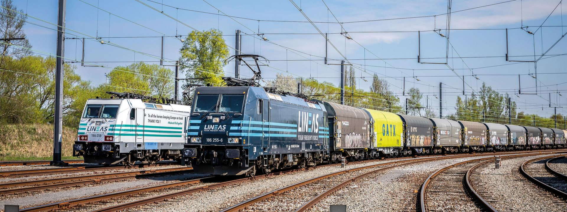 Zwei grüne und blaue Elektrolokomotiven von Lineas ziehen einen Güterzug.