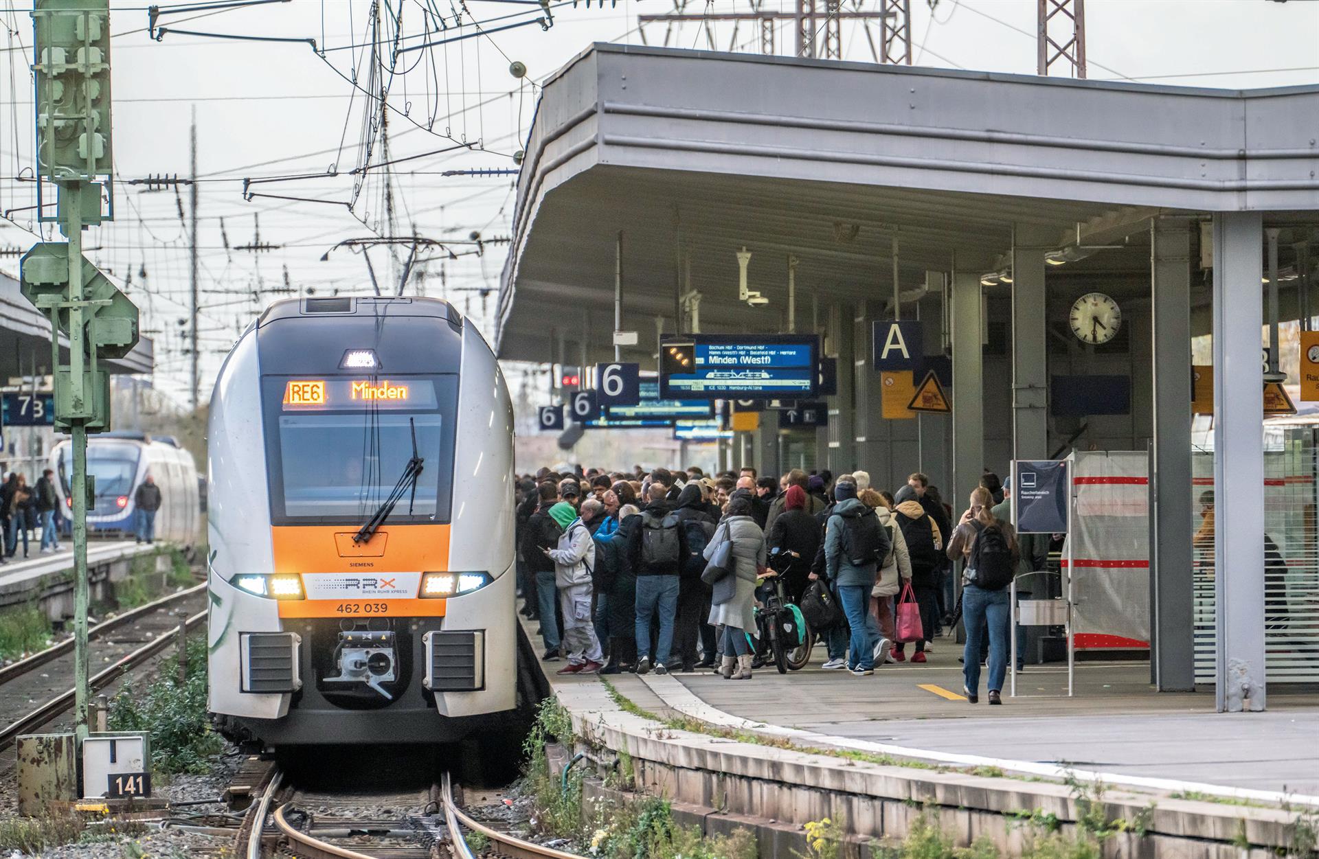 Ein voller Bahnsteig mit wartenden Menschen, während eine Regionalbahn in NRW einfahrt.