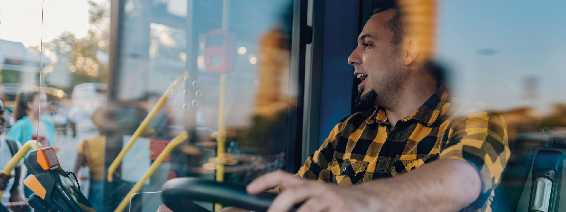 Ein Busfahrer in einem gelben Karohemd sitzt am Steuer eines Linienbusses und schaut nach vorne, symbolisierend die Transformation des öffentlichen Nahverkehrs in Richtung Klimaneutralität.