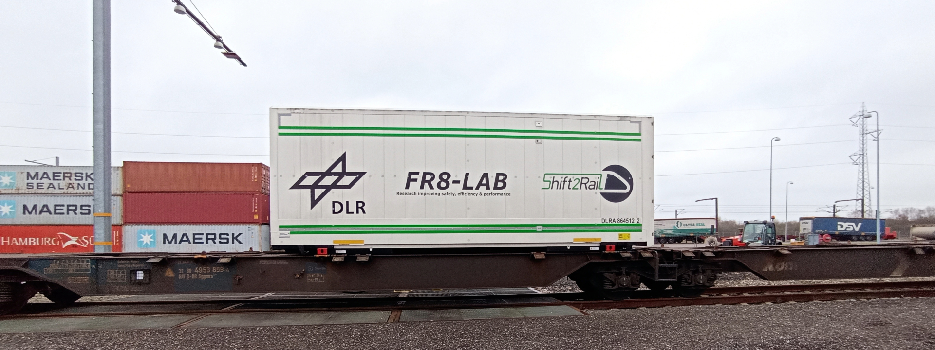 DLR-Forschungscontainer FR8-LAB auf einem Güterzug, umgeben von anderen Containern und dem Schriftzug 