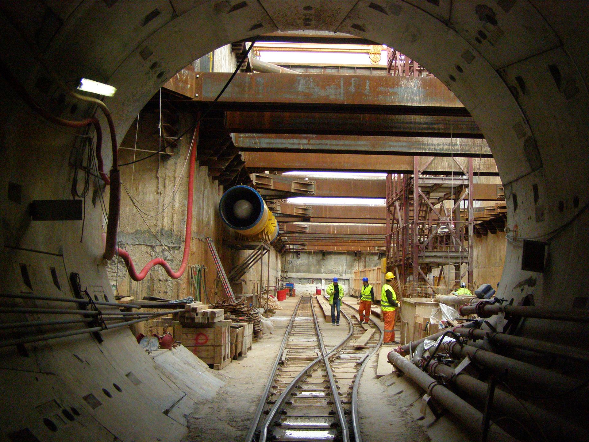 Tunnel der Metro Thessaloniki während der Bauphase. Arbeiter in Warnwesten stehen neben den Gleisen.